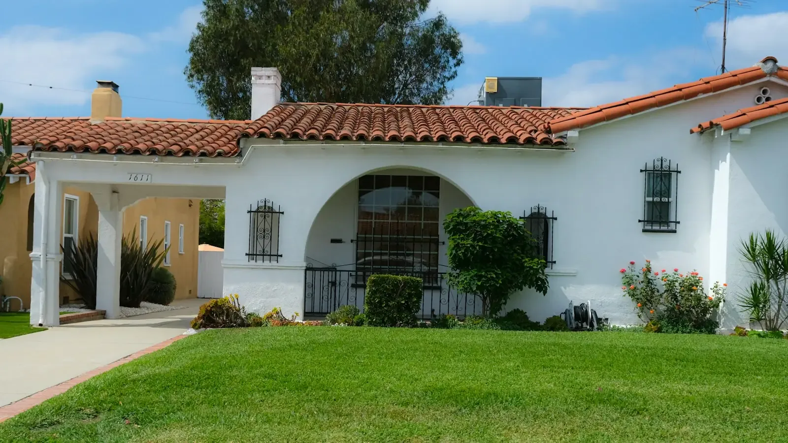 A white stucco bungalow with a red tile roof and arched entry on a Gardena street